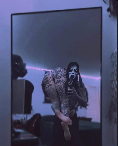 Mirror selfie by someone in a ghost face mask with a woman slung over one shoulder