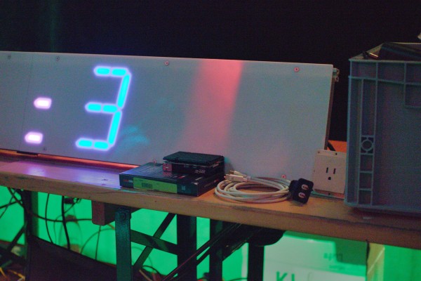 A picture of a bench, with a large LED segment showing „:3“ on top, a IEC Type B looking wall outlet insert is hidden at the right corner behind a euro-box