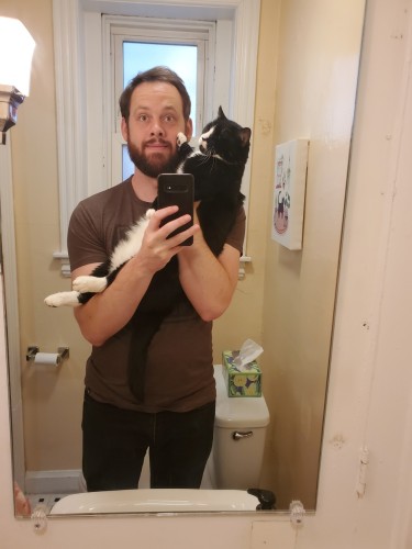 Me holding my big tuxedo cat, who is pushing his paw against my face.