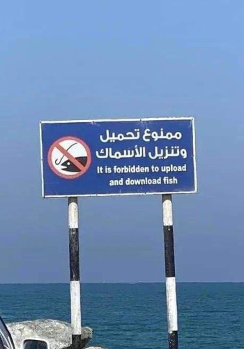 A sign with a mnemonic for "fishing forbidden" and text on it in Arabic and English: "ممنوع تحميل وتنزيل الأسماك" & "It is forbidden to upload and download fish" 