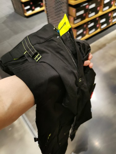 Hand holding a black pair of pants with neon yellow highlights in a clothing store