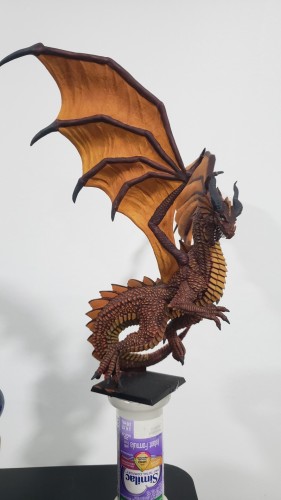 Red Dragon mini standing upright with wings spread, looking down to the right pinned to a makeshift mini holder cobbled together from a 2" square black base and an infant formula bottle filled with sand.